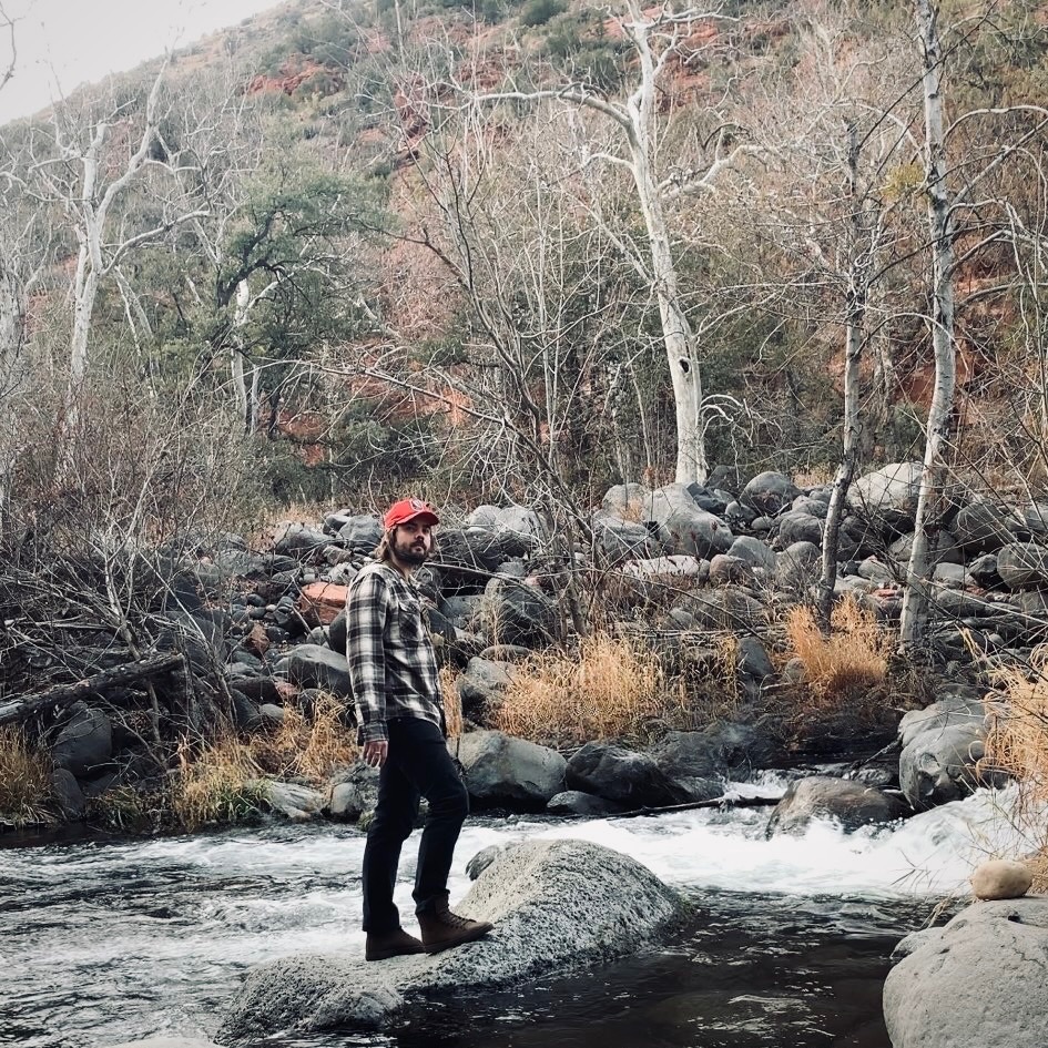 Jacob standing on a rock mid-stream in Oak Creek Canyon, sycamores and red rock behind him