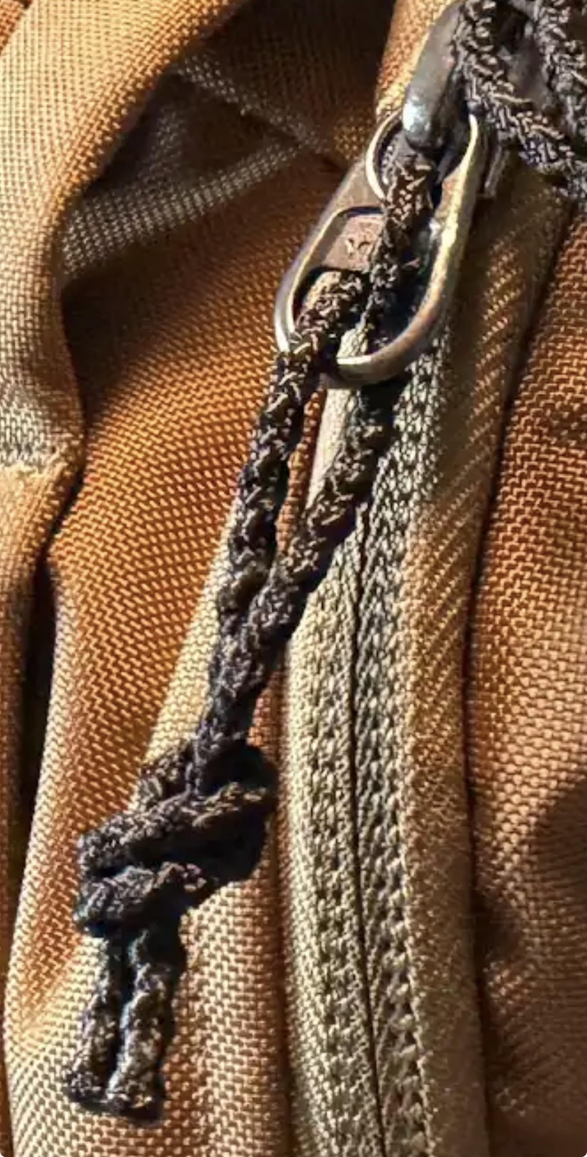 Close-up of a braided black cord zip pull knotted through a zipper slider on tan nylon